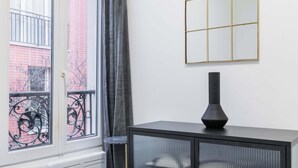 Ein Schlafzimmer mit einem Bett, einem schwarzen Schrank mit Glastüren, einem Spiegel und einem Fenster mit Blick auf ein Gebäude.