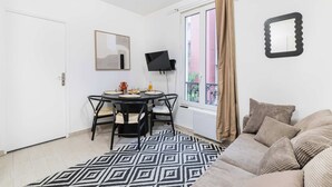 Ein Zimmer mit einem Bett, einem Esstisch mit Stühlen, einem Fernseher, einem Fenster mit Vorhängen und einem gemusterten Teppich.