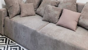 Ein Wohnzimmer mit grauem Sofa, mehreren Kissen, einem gerahmten abstrakten Gemälde und einem schwarzen abstrakten Spiegel an der Wand.