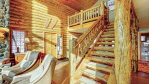 Interno di una baita in legno con una scala in legno, una zona relax con poltrone reclinabili e un muro in pietra.
