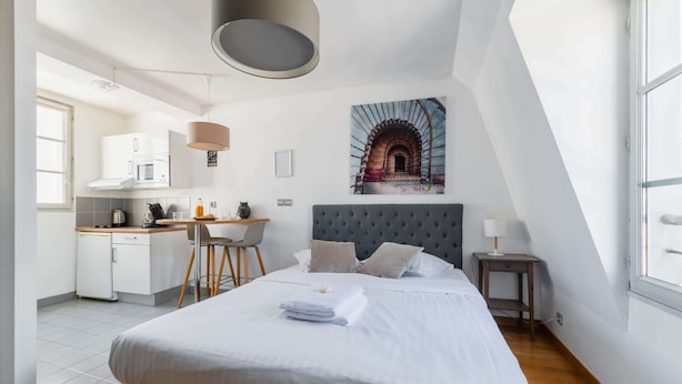 A modern room with a bed, a desk, a kitchenette, and a large window. - Jardin des Plantes View Studio w/ High-Speed WiFi (Paris)