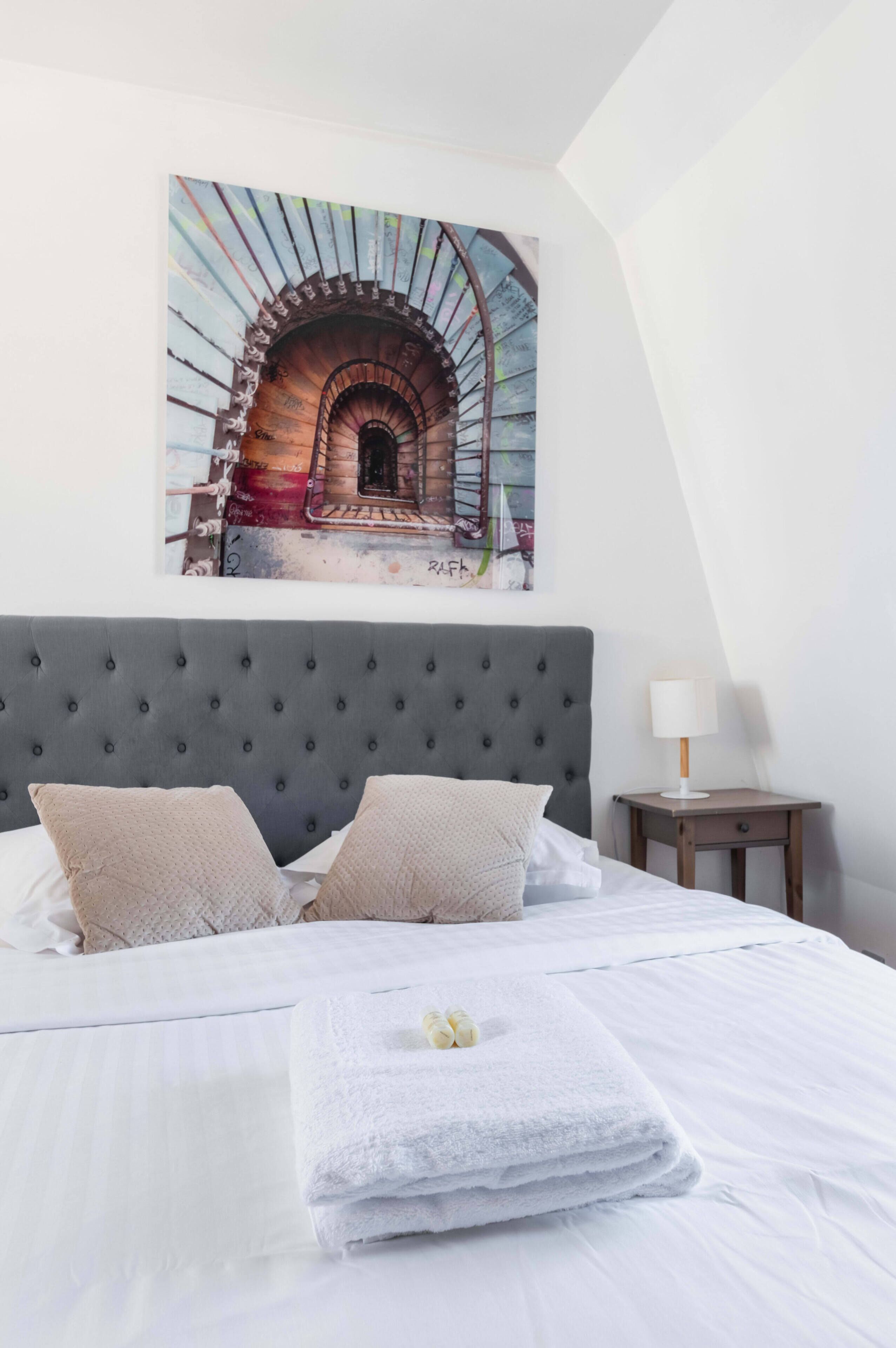 A bedroom with a large bed, a headboard, a bedside table, and a wall-mounted artwork.