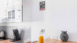 A modern kitchen with a round wooden table, a coffee maker, a bottle of orange juice, and a plate of croissants. - Jardin des Plantes View Studio w/ High-Speed WiFi (Paris)