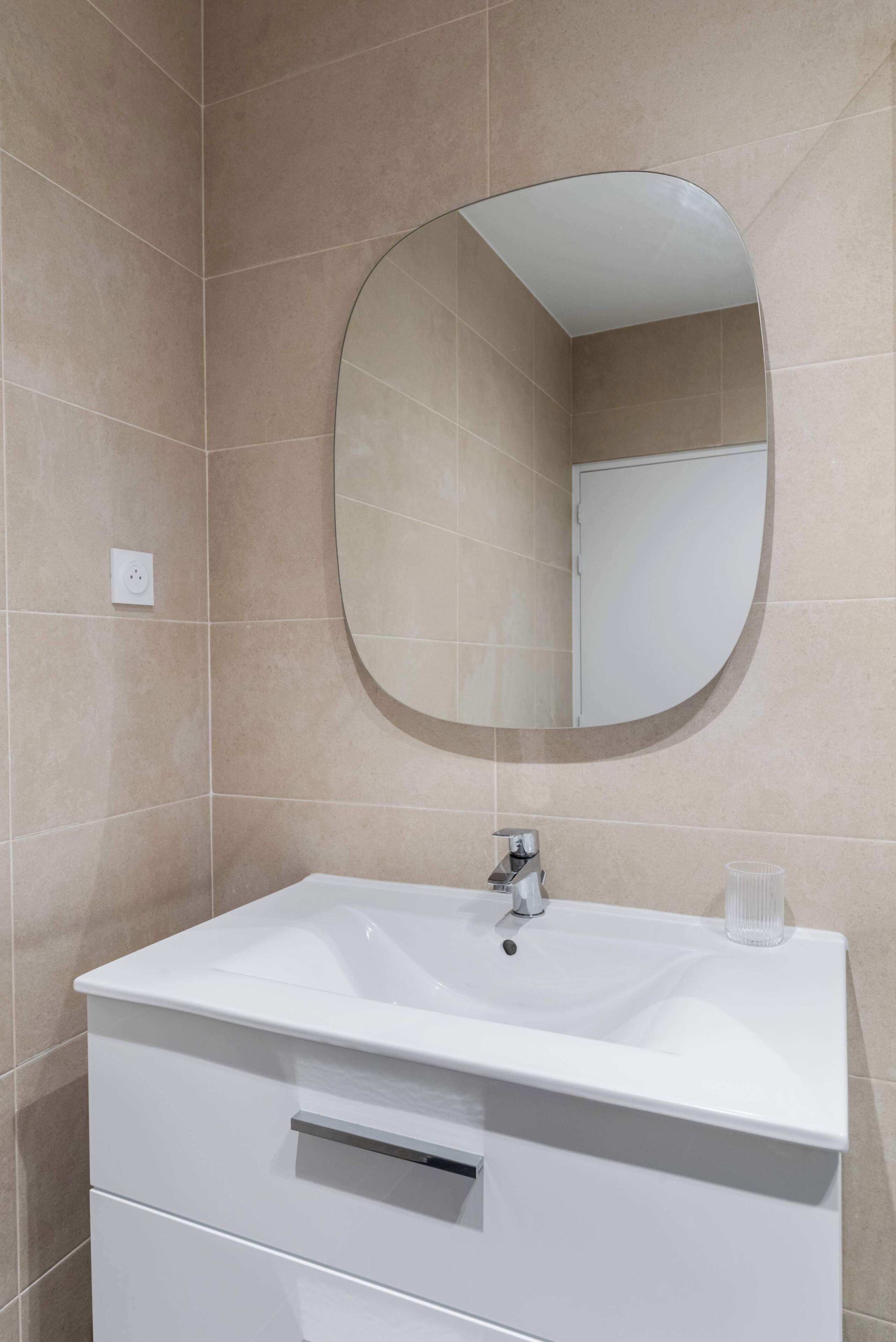 A bathroom with a white sink, a round mirror, and beige tiled walls.