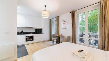 Une chambre d’hôtel avec un lit, une petite table avec des chaises, un coin cuisine et une fenêtre avec des rideaux.