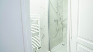 A glass-enclosed shower area with a white tiled wall and a white door. - Logement cosy metro Pierre Lachaise - 3P (Paris)