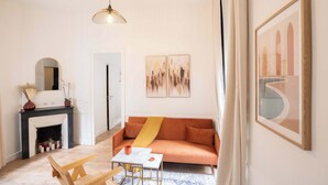 A living room with a sofa, a small table, a fireplace, and artwork on the walls. - Logement cosy metro Pierre Lachaise - 3P (Paris)