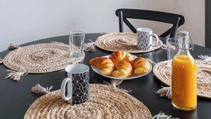 A dining table with placemats, a glass of juice, a plate of croissants, and a framed abstract artwork on the wall. - Appartement lumineux avec terrasse Courbevoie - 4P (Courbevoie)