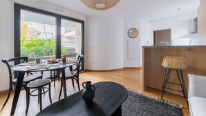 A modern kitchen with a wooden countertop and a round island, a dining area with a black table and chairs, and a large window with a view of greenery. - Appartement lumineux avec terrasse Courbevoie - 4P (Courbevoie)