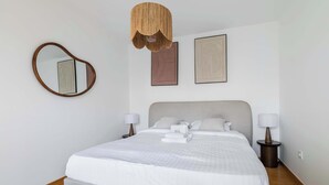 A neatly made bed with white linens, a round mirror on the wall, and two bedside lamps. - Appartement lumineux avec terrasse Courbevoie - 4P (Courbevoie)