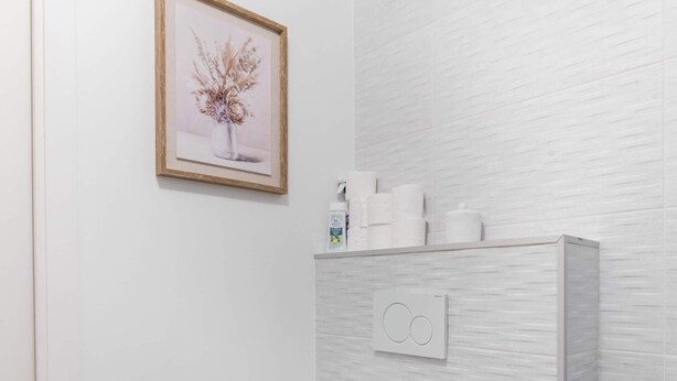 Ein Badezimmer mit Toilette, einem gerahmten Bild an der Wand und einem Ablagefach mit Pflegeprodukten.