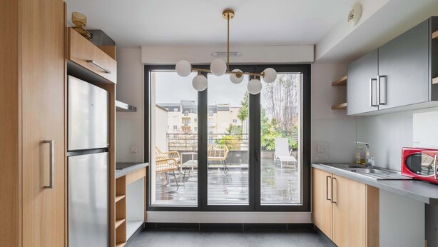 Una cocina moderna con un amplio ventanal corredera, electrodomésticos de acero inoxidable y un microondas rojo.