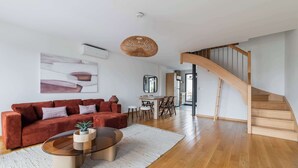 Una sala de estar moderna con un sofá rojo, una mesa de centro de vidrio, una lámpara de techo tejida y una escalera de madera.
