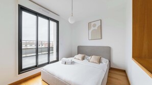 Un dormitorio moderno con un ventanal grande, una cama con almohadas, una mesita de noche y una obra de arte en la pared.