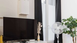 A modern room with a flat-screen TV, a white table with breakfast items, a fan, and a potted plant. - Studio agreable et bien placee - Paris 18 - 2P (Paris)