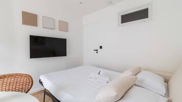 A hotel room with a bed, a flat-screen TV, a wall-mounted light switch, and a small window.