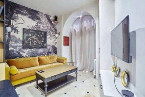Un salon avec un canapé, une table basse, un téléviseur et une fresque murale.