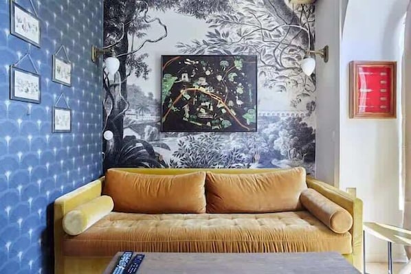 Une pièce avec un mur orné de motifs, un canapé avec des coussins, un tableau encadré et une lampe.