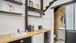 A modern kitchen with a sink, microwave, and coffee maker on the counter. There are shelves above the counter with decorative items and a small potted plant.