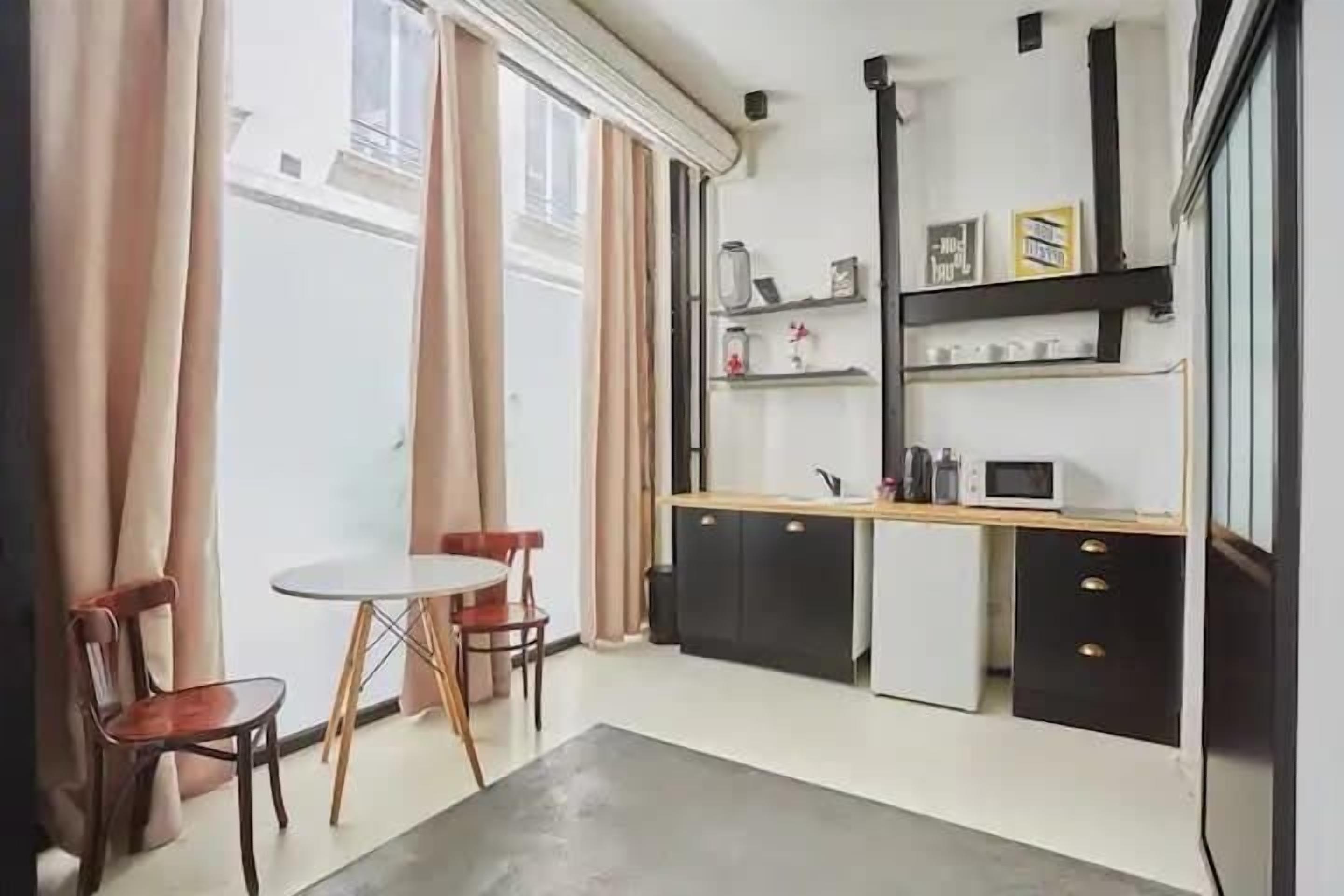 Een kleine keuken met een eettafel en stoelen, een kleine koelkast, en een magnetron.