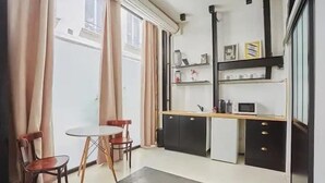 A compact kitchen with a dining table and chairs, a small refrigerator, and a microwave.
