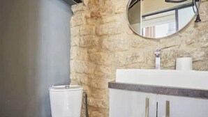A bathroom with a stone wall, a toilet, a sink with a mirror, and a towel dispenser.
