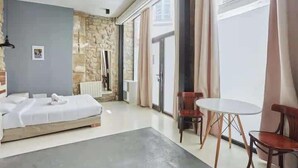 A hotel room with a bed, a small table, chairs, a stone accent wall, and a view through a window.