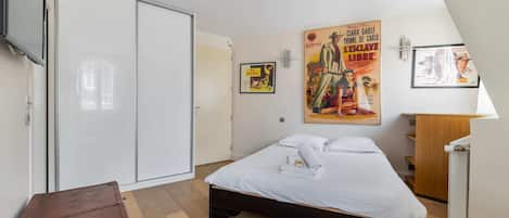 Un dormitorio con una cama, un aparador de madera, un armario y un póster en la pared.