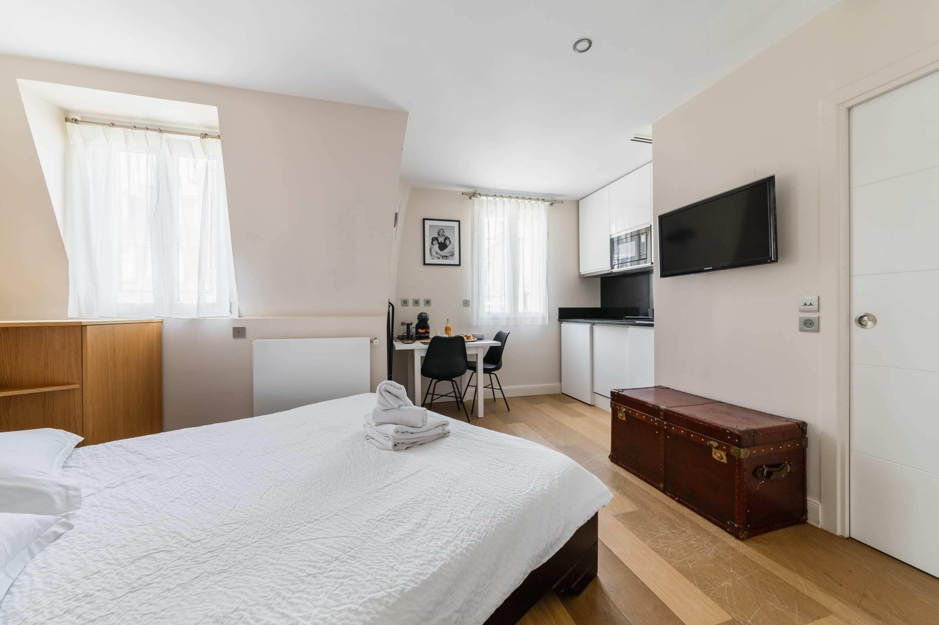 A hotel room with a bed, a desk, a chair, a television, and a suitcase.