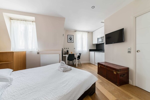 Une chambre d’hôtel avec un lit, un bureau, une chaise, une télévision et une valise.