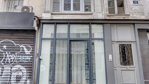Eine Gebäudefassade mit einer großen Glasdoor, einem geschlossenen Rollladen mit Graffiti und einem kleinen Fenster mit aufwendigen Metallgitter.