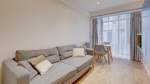 Ein stilvolles Wohnzimmer mit einem grauen Sofa, einem Esstisch mit Stühlen und einem großen Fenster mit Vorhängen.