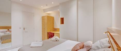 A modern bedroom with a large bed, a wooden wardrobe, a mirror, and a small desk.