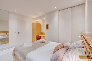 Une chambre moderne avec un grand lit, une armoire en bois, un miroir et un petit bureau.