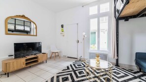 Ein Wohnzimmer mit Fernseher, einer Holz-Unterhaltungsecke, einem gemusterten Teppich, einem runden Glastisch und einem blauen Sofa.