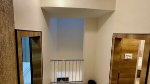 A spacious hallway with a high ceiling, a visible light fixture, and a metal railing. - Greystone 4BHK Pvt Pool by Stellar Stays (Mawal)