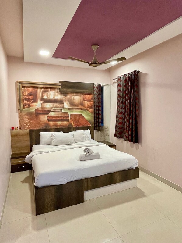 A hotel room with a large bed, a ceiling fan, a wall-mounted TV, and a window with patterned curtains. - Greystone 4BHK Pvt Pool by Stellar Stays (Mawal)