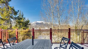 Un espace extérieur aménagé avec une table et des chaises en métal, une clôture rouge et une vue sur des montagnes enneigées.