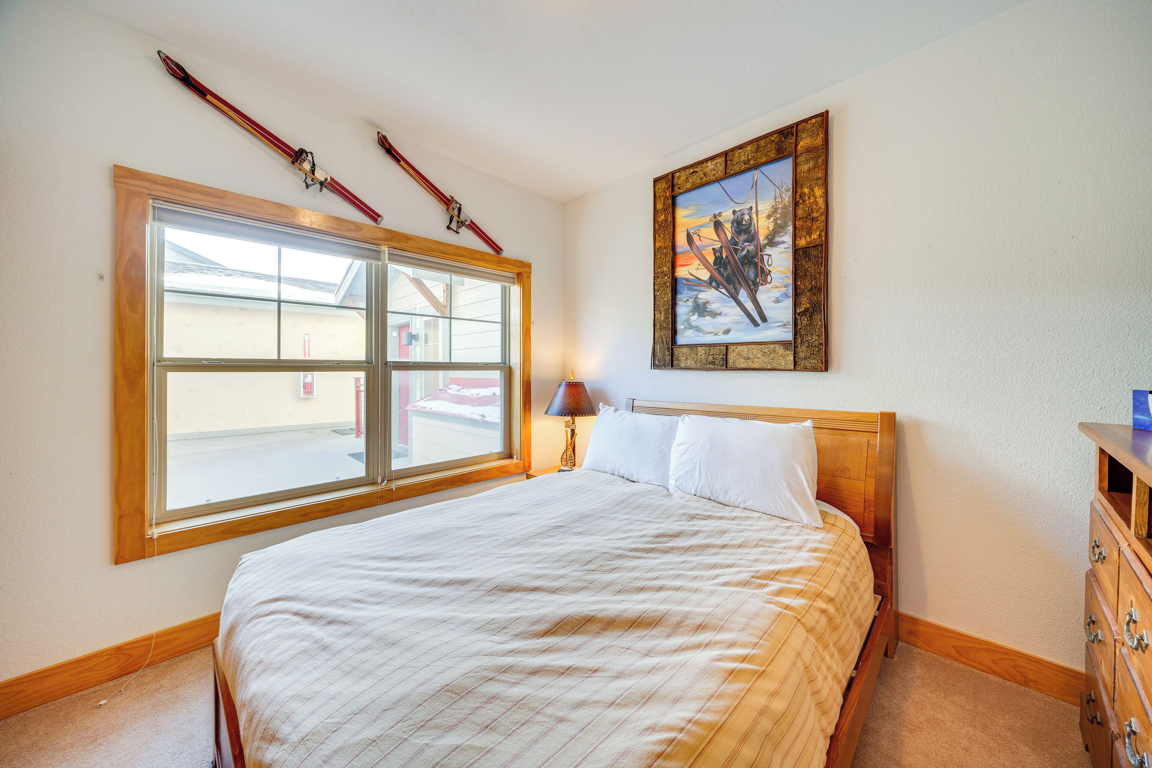 Un dormitorio con un ventanal grande, una cama, un aparador y un cuadro en la pared.