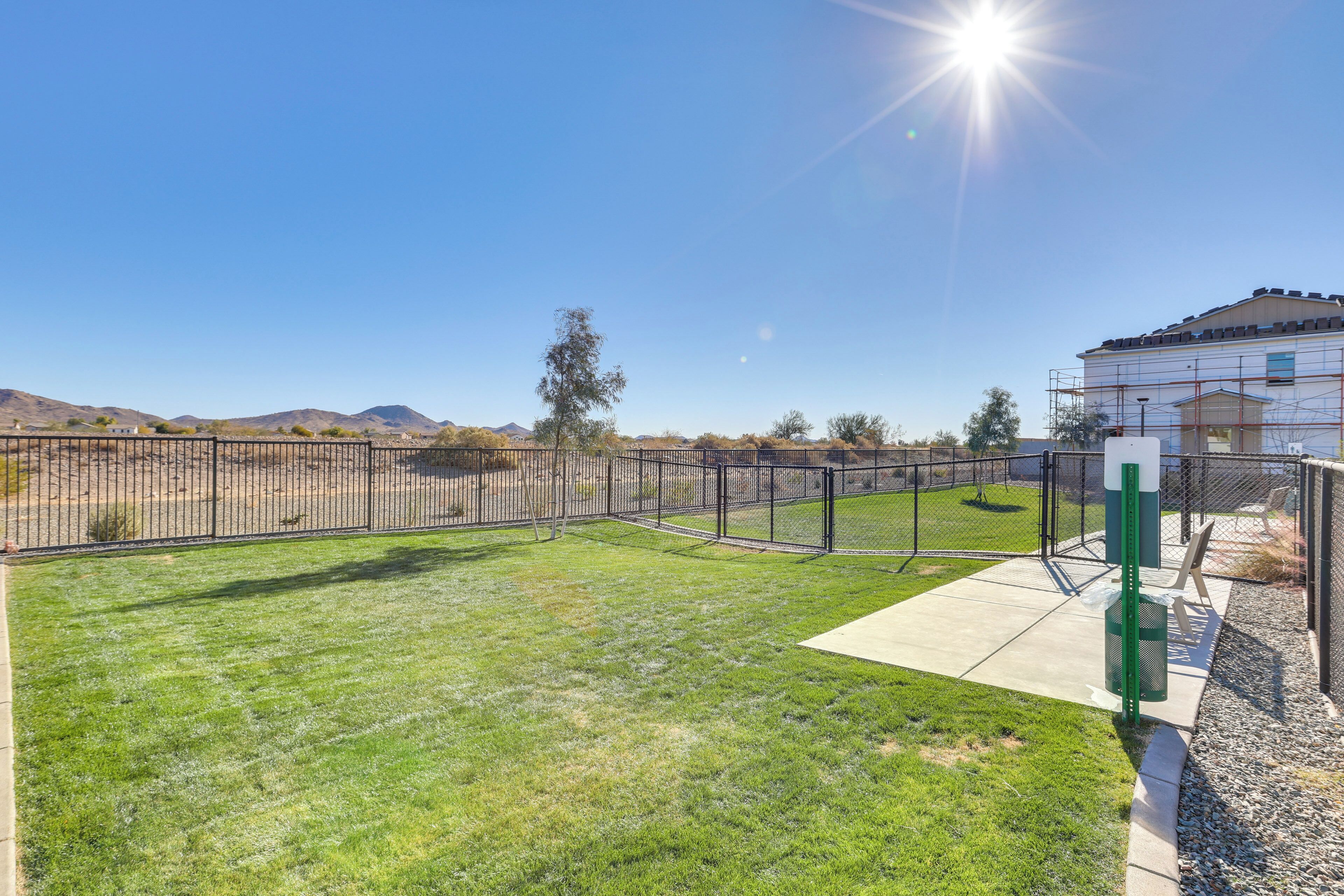 A fenced backyard with a grassy lawn, a concrete patio, and a building under construction.