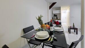 Un comedor moderno con una mesa de vidrio dispuesta para dos personas, con platos, cubiertos y una botella de vino.