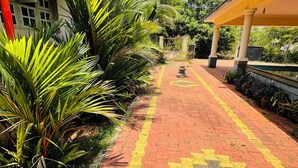 Uma passagem pavimentada com um padrão amarelo e vermelho, ladeada por palmeiras e um edifício com toldo amarelo.