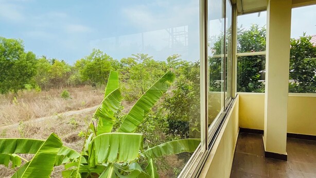 Quarto com grandes janelas que oferecem vista para um jardim exuberante e árvores distantes.
