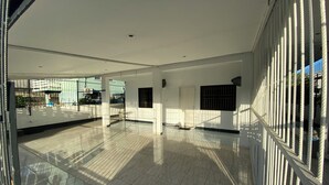 A spacious indoor area with a tiled floor, large windows, and a metal railing.