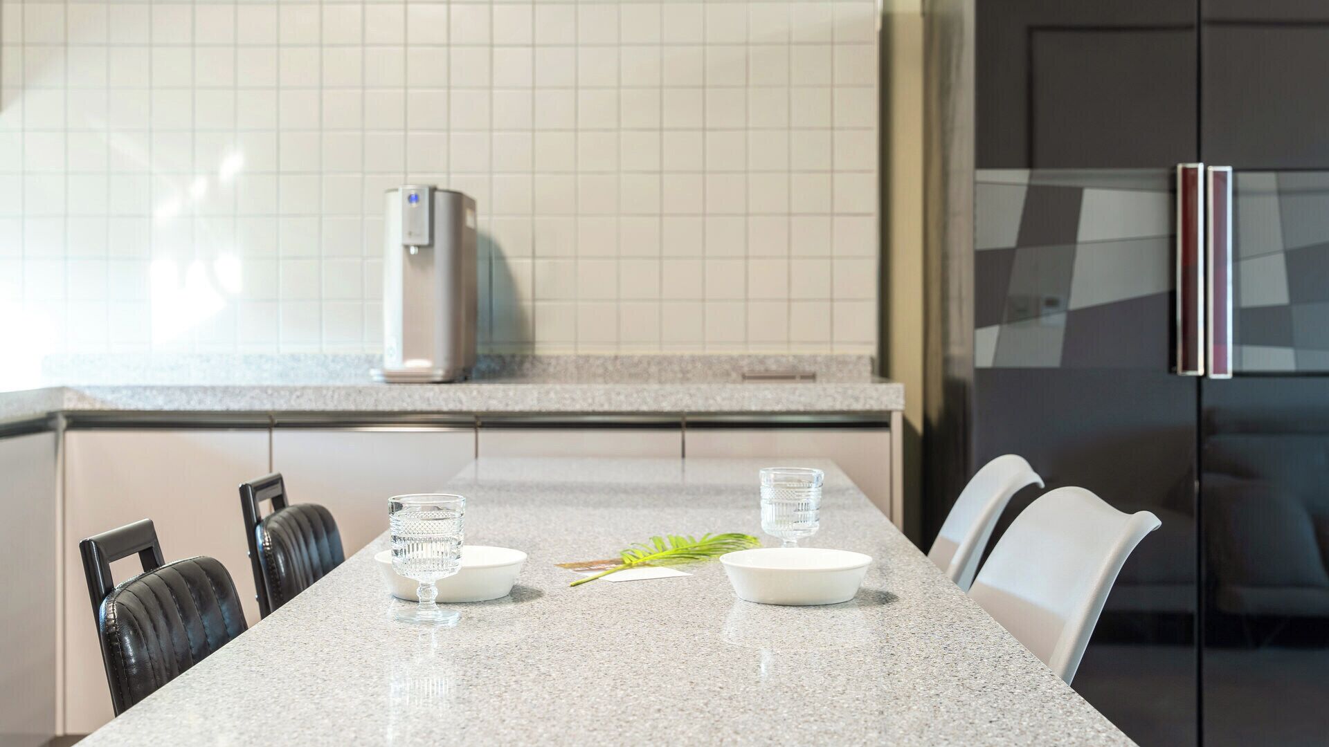Une cuisine moderne dotée d’un comptoir en granit, d’appareils électroménagers en acier inoxydable et d’un coin repas avec des chaises et une table dressée pour deux personnes.