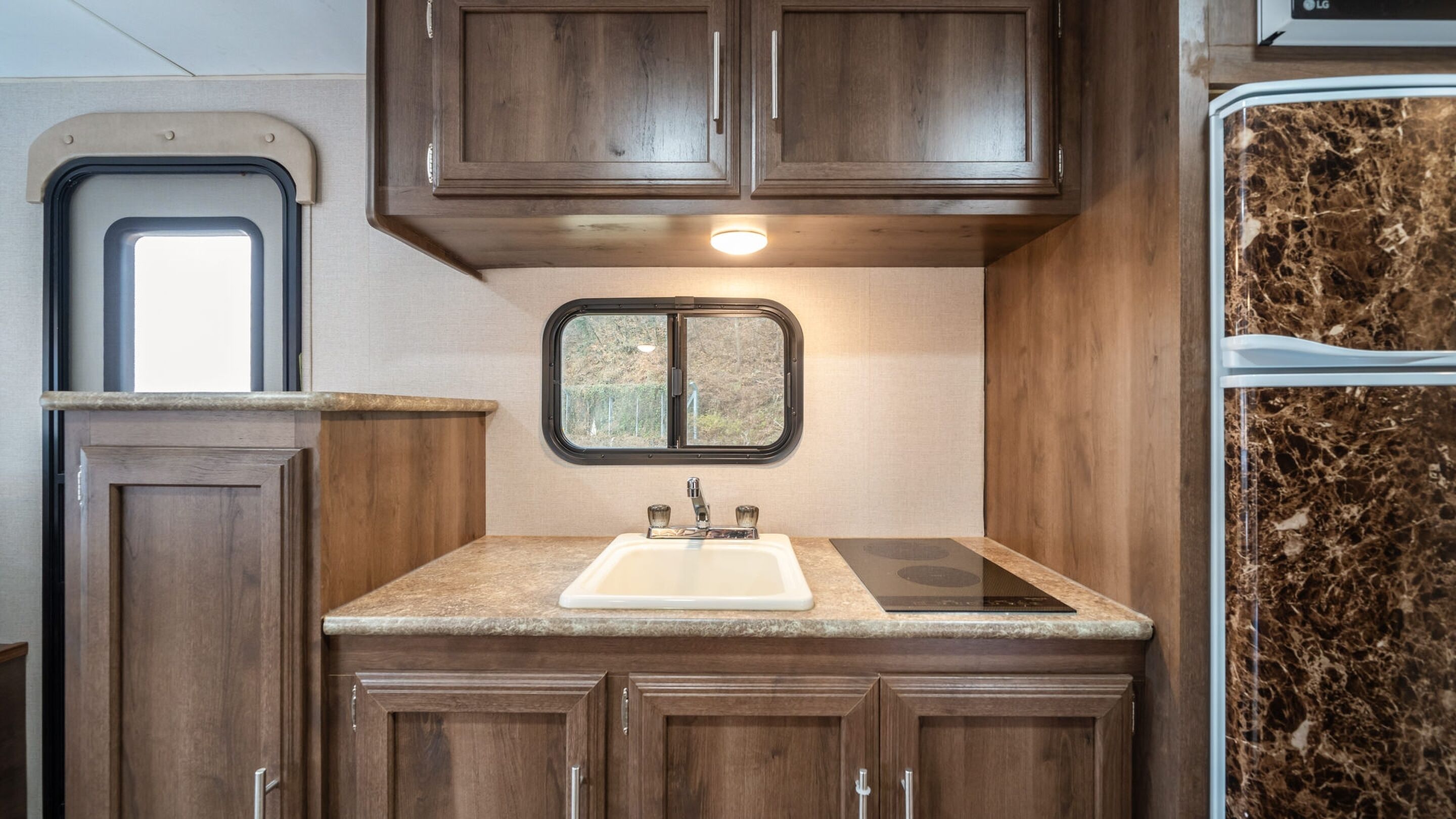 A compact kitchen with dark wood cabinets, a granite countertop, a double sink, and a window with a view of greenery.