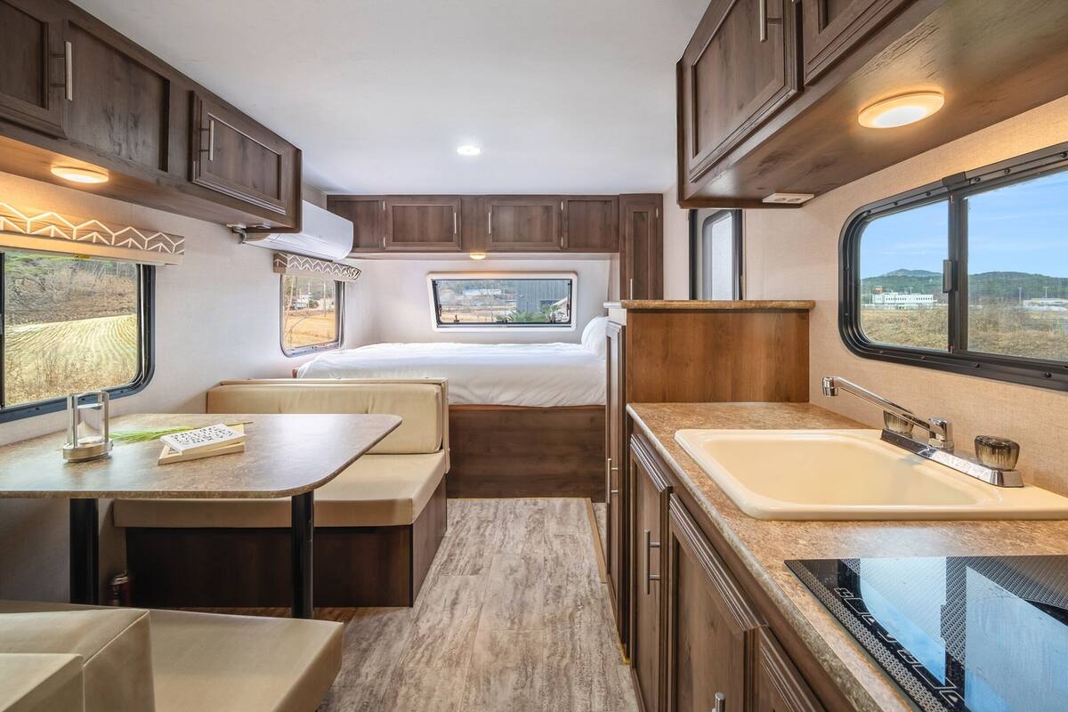 Un intérieur de camping-car compact comprenant un coin cuisine, un espace repas, un lit et une fenêtre offrant une vue sur l’extérieur.