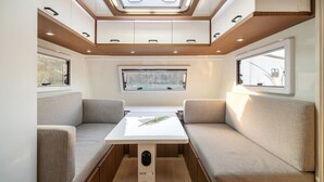A cozy RV interior with a central table, cushioned seating, and a skylight. - Goseong Hoostay Caravan Pension (Goseong)
