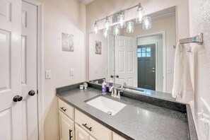A bathroom with a white sink, a large mirror, and a countertop with a soap dispenser and a bottle.