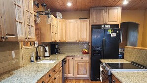 Eine Küche mit Holzausstattung, Granit Arbeitsplatten, einem schwarzen Kühlschrank und einer Kaffeemaschine.